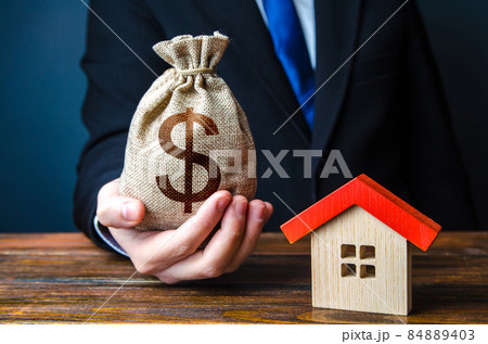 Man holds out a money bag near the house. Bank approval for issuing a mortgage loan. Favorable terms and conditions, low interest rate. Home purchase, invest in real estate. Property appraisal. 84889403