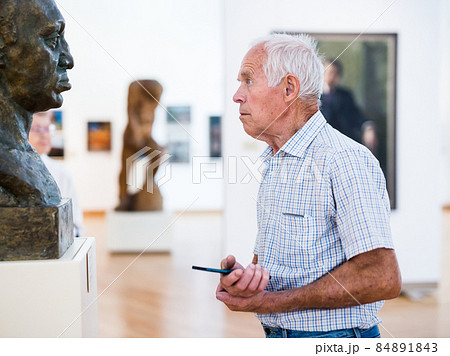mature European man examines sculpture in an exhibition in hall of an art museum 84891843