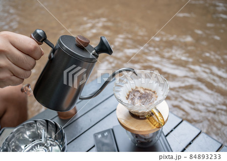 Man dripping hot coffee and camping near river at nature park. Outdoor activity and relax on holiday. 84893233