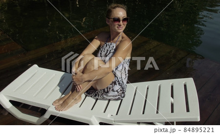 Woman lie on a sunbed in sunglasses and a boho silk shawl. Girl rest on a flood wood underwater pier. The pavement is covered with water in the lake. Woman lie on a sunbed in sunglasses and a boho silk shawl. Girl rest on a flood wood underwater pier. The pavement is covered with water in the lake. 84895221