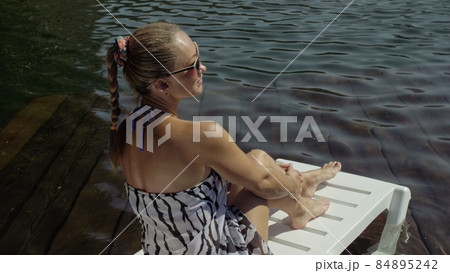 Woman lie on a sunbed in sunglasses and a boho silk shawl. Girl rest on a flood wood underwater pier. The pavement is covered with water in the lake. Woman lie on a sunbed in sunglasses and a boho silk shawl. Girl rest on a flood wood underwater pier. The pavement is covered with water in the lake. 84895242