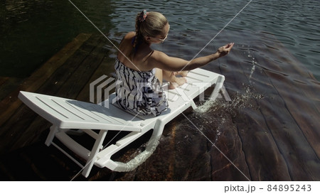 Woman lie on a sunbed in sunglasses and a boho silk shawl. Girl rest on a flood wood underwater pier. The pavement is covered with water in the lake. Woman lie on a sunbed in sunglasses and a boho silk shawl. Girl rest on a flood wood underwater pier. The pavement is covered with water in the lake. 84895243