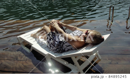Woman lie on a sunbed in sunglasses and a boho silk shawl. Girl rest on a flood wood underwater pier. The pavement is covered with water in the lake. Woman lie on a sunbed in sunglasses and a boho silk shawl. Girl rest on a flood wood underwater pier. The pavement is covered with water in the lake. 84895245
