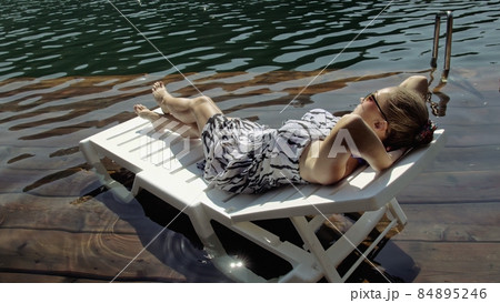 Woman lie on a sunbed in sunglasses and a boho silk shawl. Girl rest on a flood wood underwater pier. The pavement is covered with water in the lake. Woman lie on a sunbed in sunglasses and a boho silk shawl. Girl rest on a flood wood underwater pier. The pavement is covered with water in the lake. 84895246