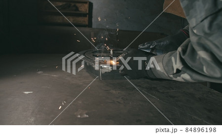 Forge workshop. Smithy. Worker in a welding hood helmet welds a part by electric welding. Sparks are reflected in the protective screen. 84896198