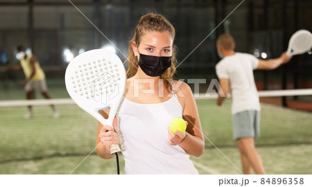 Portrait of woman in protective mask with racket and ball in his hands on the padel court 84896358