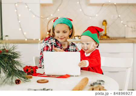 Brother and sister are sitting in the kitchen and congratulating their grandparents on Christmas and New Year via video link. Remote celebration of the online Christmas holiday 84896927