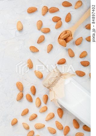 Milk from organic almonds in a transparent bottle with a scattering of seeds and a wooden spoon on a light background 84897402