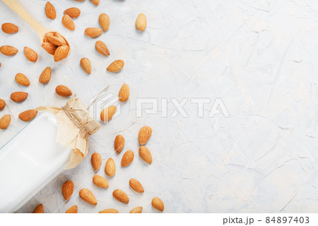 Almond milk in a glass bottle on a light background with a scattering of seed kernels and a wooden spoon. 84897403