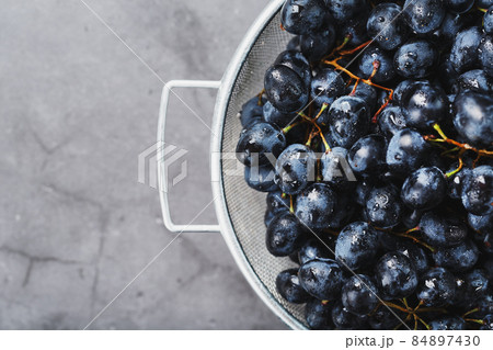 Ripe black grapes in a metal bowl on a black background. 84897430