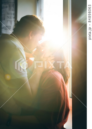Portrait of a couple kissing against the backdrop of the sunset illuminating the camera. Front view. 84898063