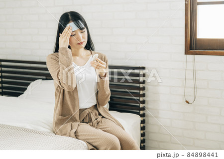 ベッドで休む体調不良の女性(冷却シート・体温計・困る) ベッドで休む体調不良の女性(冷却シート・体温計・困る) 84898441