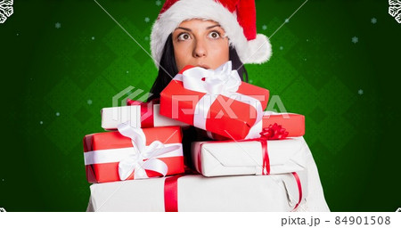 Thoughtful woman in santa hat with stack of christmas presents against green background, copy space 84901508