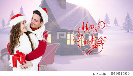 Happy couple in santa hats holding gift by christmas greeting while snow covered house in background Happy couple in santa hats holding gift by christmas greeting while snow covered house in background 84901509