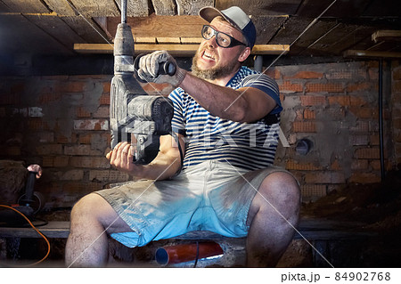 Funny bearded man with heavy duty perforator in the basement of the house 84902768