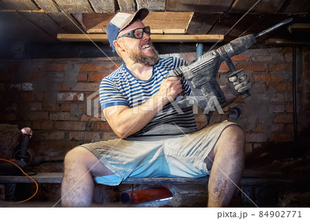 Funny bearded man with heavy duty perforator in the basement of the house Funny bearded man with heavy duty perforator in the basement of the house 84902771