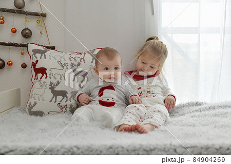 Brother and sister in Christmas pajamas are sitting on the bed. 84904269