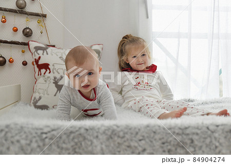Brother and sister in Christmas pajamas are sitting on the bed. Brother and sister in Christmas pajamas are sitting on the bed. 84904274