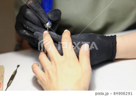 Nail master using electrical equipment to clean client nails in modern beauty studio 84906291