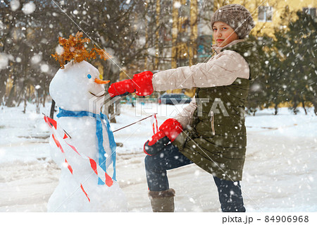 a girl plays with snow on a city street and makes a snowman 84906968