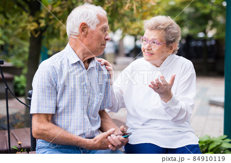mature man with a woman sitting on bench in spring mature man with a woman sitting on bench in spring 84910119