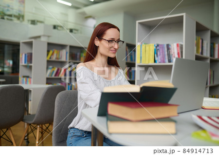 Woman with glasses working at laptop in library 84914713