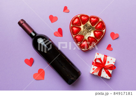 Bottle of red wine on colored background for Valentine Day with gift and chocolate. Heart shaped with gift box of chocolates top view with copy space Bottle of red wine on colored background for Valentine Day with gift and chocolate. Heart shaped with gift box of chocolates top view with copy space 84917181
