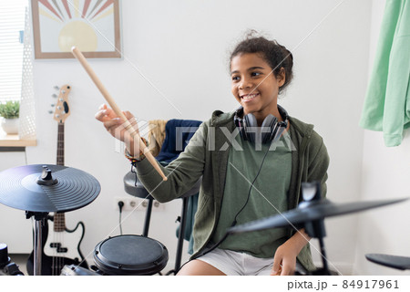 Happy cute schoolgirl with drumsticks hitting drums at lesson of music Happy cute schoolgirl with drumsticks hitting drums at lesson of music 84917961