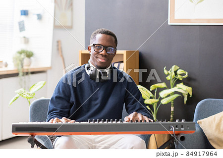 Happy young man in eyeglasses and casualwear sitting by piano keyboard Happy young man in eyeglasses and casualwear sitting by piano keyboard 84917964