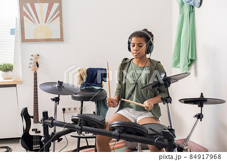 Youthful girl in headphones sitting by drumkit in front of smartphone camera Youthful girl in headphones sitting by drumkit in front of smartphone camera 84917968