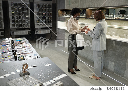 Two young well-dressed women in masks standing by large display Two young well-dressed women in masks standing by large display 84918111