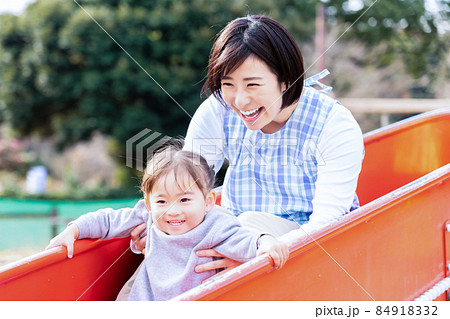 滑り台で遊ぶ2歳児の女の子と若い女性の保育士 84918332