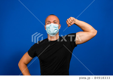 Man with protective mask showing muscles on blue background. Strong immunity concept 84918333