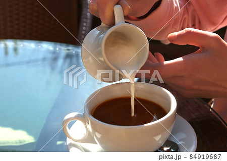 Woman pouring milk in coffee at table in cafe Woman pouring milk in coffee at table in cafe 84919687