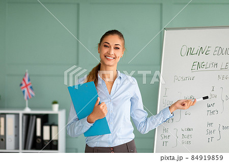 Training concept. Cheerful female tutor teaching English language, pointing at grammar rules on board 84919859