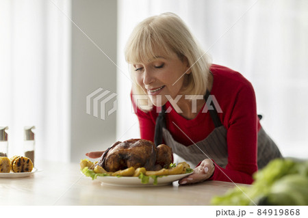 Beautiful senior woman smelling tasty roasted turkey, cooking festive Christmas dinner for her family in kitchen, copy space 84919868