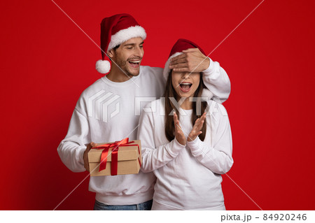 Cheerful Young Man In Santa Hat Making Christmas Surprise To Excited Girlfriend 84920246