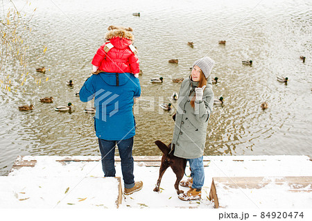 Full height family portrait with one kid and dog in winter casual outfit posing outdoors 84920474