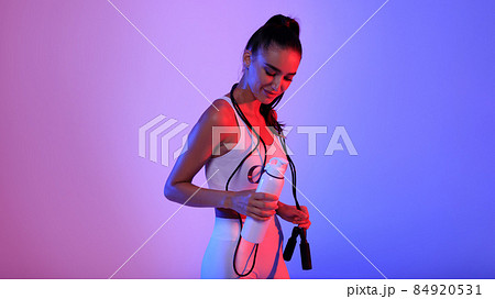 Sporty Female With Jump Rope Holding Bottle Standing, Neon Background 84920531