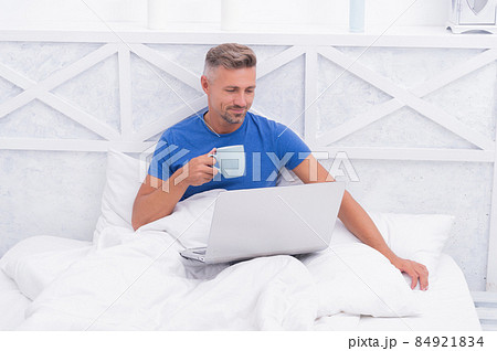 Awake from sleep. Awake man in bed. Happy guy drink tea using laptop. Morning relaxation 84921834