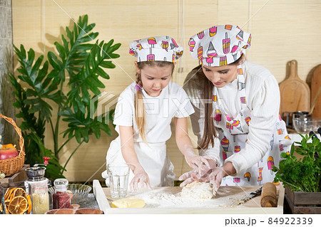 In one of the last stages, mother and daughter knead and knead a cake that will serve as a pizza cake. Mother and baby do the dough together in the kitchen. In one of the last stages, mother and daughter knead and knead a cake that will serve as a pizza cake. Mother and baby do the dough together in the kitchen. 84922339