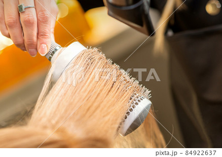 Hairdresser hand drying blond hair with a hairdryer and round brush in a beauty salon. 84922637