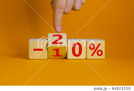 Hand turns a cube and changes the expression '-10 percent' to '-20 percent'. Beautiful orange background, copy space. Business concept. Hand turns a cube and changes the expression '-10 percent' to '-20 percent'. Beautiful orange background, copy space. Business concept. 84923550