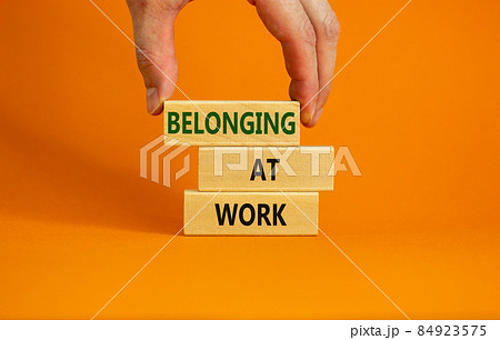 Belonging at work symbol. Wooden blocks with words 'Belonging at work' on beautiful orange background. Businessman hand. Business, belonging at work concept. Copy space. Belonging at work symbol. Wooden blocks with words 'Belonging at work' on beautiful orange background. Businessman hand. Business, belonging at work concept. Copy space. 84923575