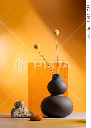 Dry yellow flowers on a trend black vase on orange background with orange glass Dry yellow flowers on a trend black vase on orange background with orange glass 84924783