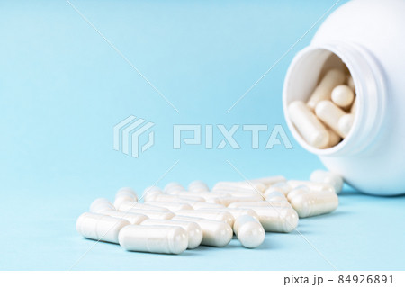 White medical pills and capsules spilling out of bottle. Medication in white container on blue background. White medical pills and capsules spilling out of bottle. Medication in white container on blue background. 84926891