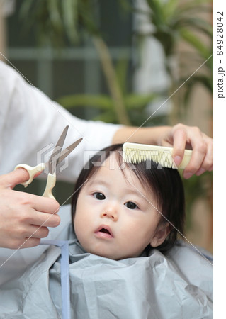 ママに前髪を切って貰う赤ちゃんの女の子の写真素材