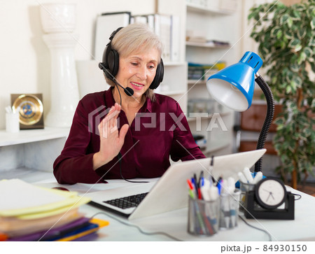 Elderly businesswoman in headphones holding video meeting with customer 84930150