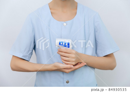 Temperature measurement gun in doctor hands. Close-up shot of doctor wearing protective surgical mask ready to use infrared isometric thermometer gun to check body temperature for virus symptoms. Temperature measurement gun in doctor hands. Close-up shot of doctor wearing protective surgical mask ready to use infrared isometric thermometer gun to check body temperature for virus symptoms. 84930535