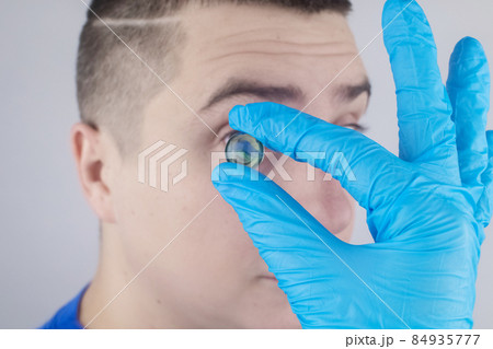 Conceptual shot of an eye crystalline lens replacement. Ophthalmic surgery. Return of sight. Removal of cataracts. Surgical intervention in the eyeball. Doctor holds the implant near the patient Conceptual shot of an eye crystalline lens replacement. Ophthalmic surgery. Return of sight. Removal of cataracts. Surgical intervention in the eyeball. Doctor holds the implant near the patient 84935777